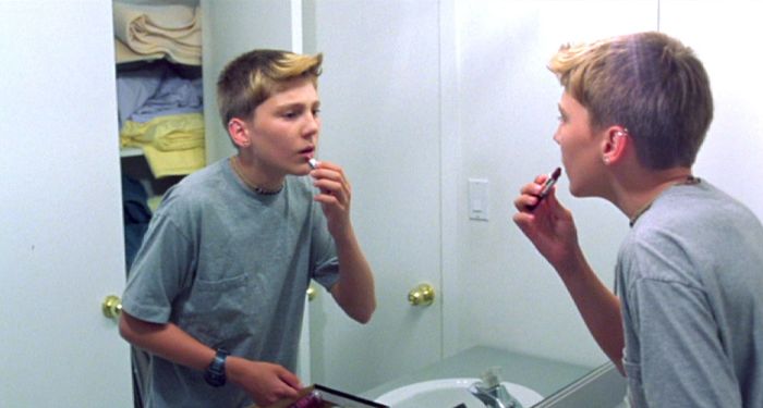 A still from L.I.E. (2001) featuring Paul Dano as Howie Blitzer, applying lipstick in front of a mirror, symbolizing his struggle with identity, self-expression, and the complexities of coming-of-age.