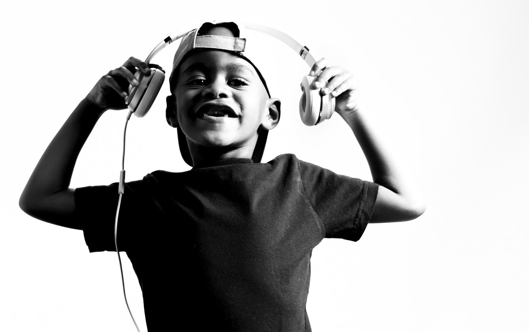 A young DJ Arch Jnr grinning while holding white headphones above his head