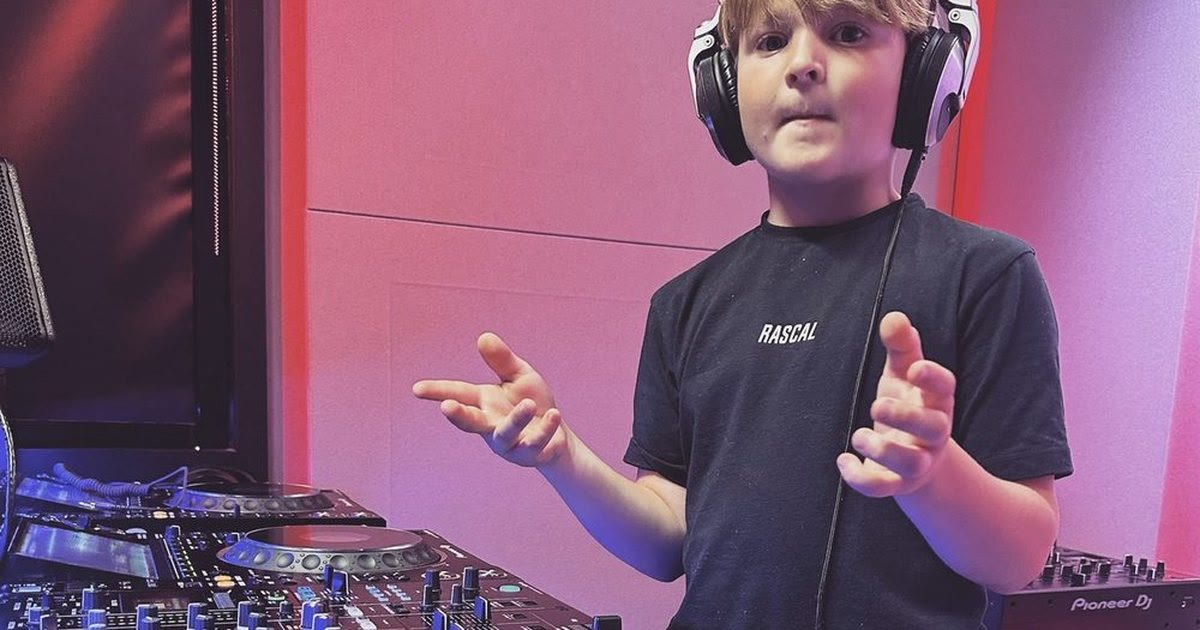 DJ Archie wearing headphones, hands raised over a Pioneer DJ setup