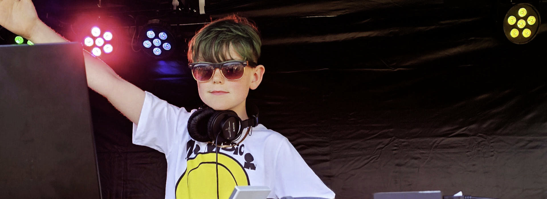 Efan Electro performing on an outdoor stage, headphones around his neck, one arm raised