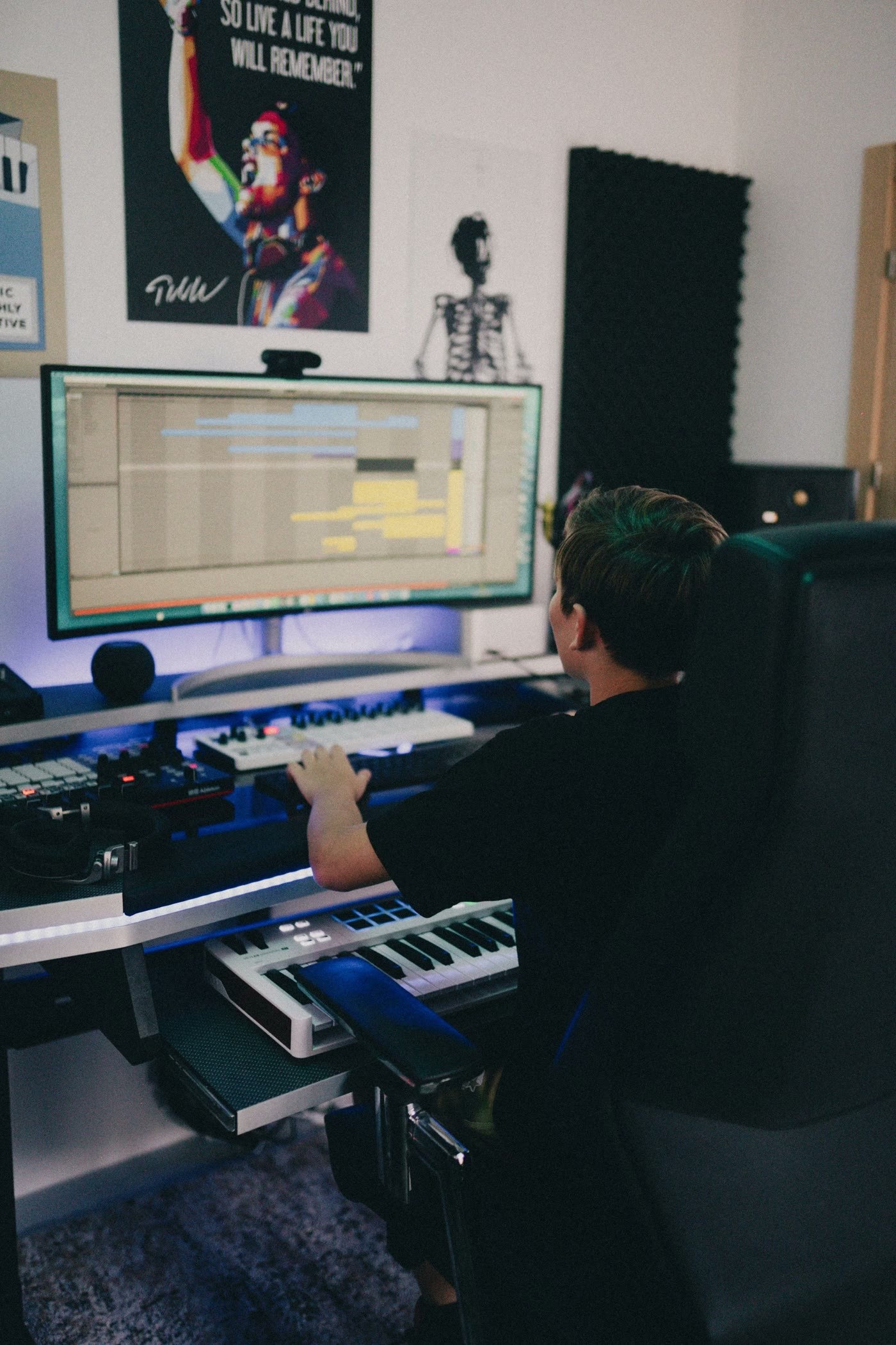 ELFIGO seen from behind at his studio desk, a DAW session on the monitor and a MIDI keyboard under his hand
