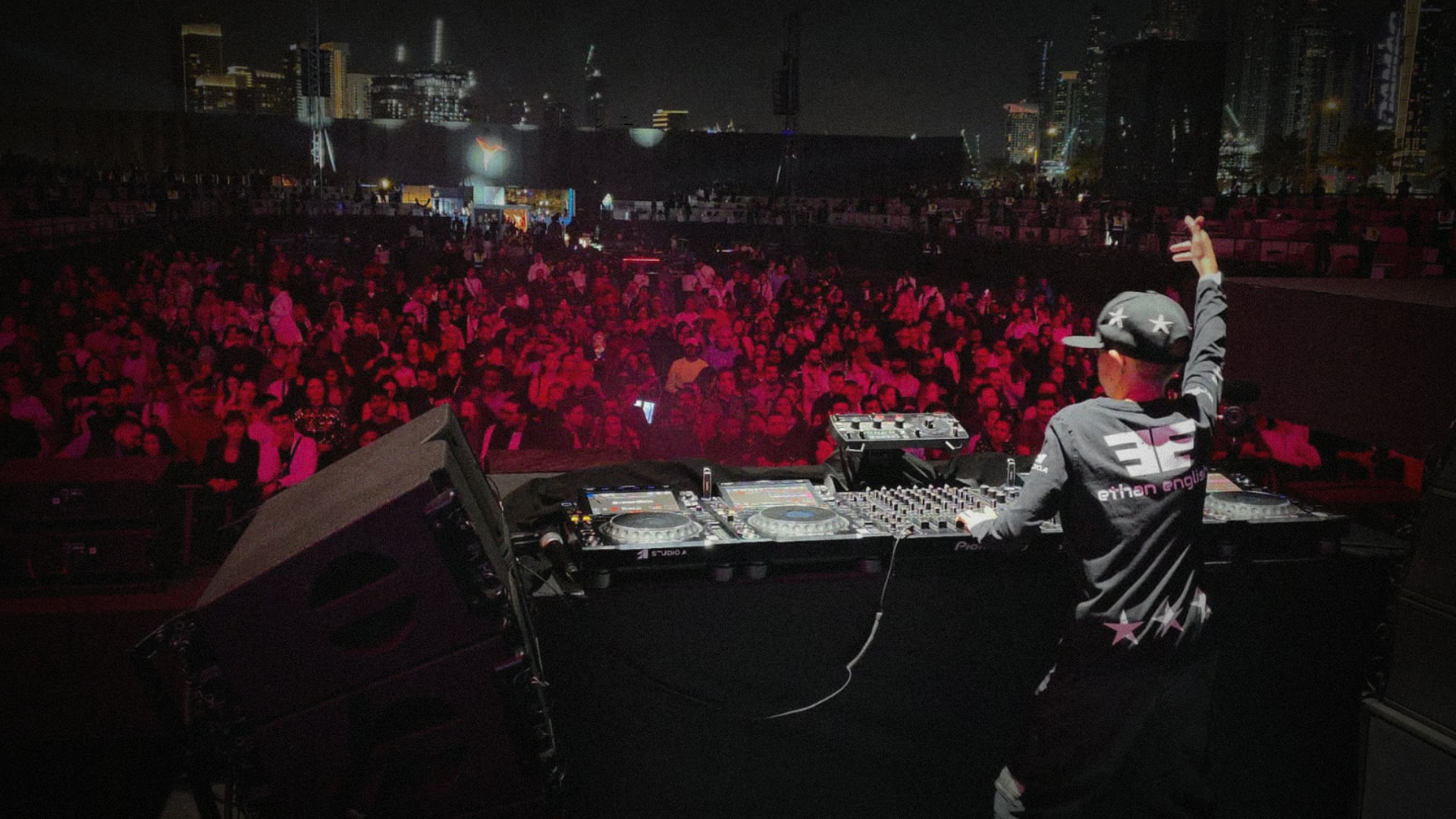 Ethan English seen from behind on an outdoor night stage, facing a large crowd