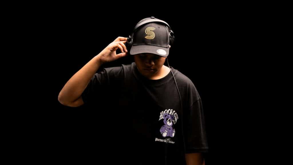 Jeremy Gomez in a black cap, holding his headphones against a black background